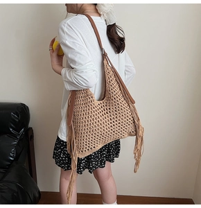 Detail of hand-woven straw tote bag with long side tassels and brown leather shoulder strap