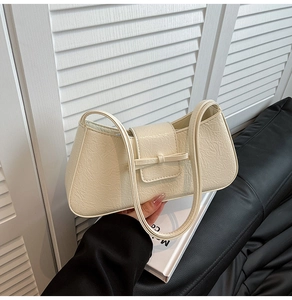 Detail of cream pleated baguette bag featuring a delicate leather bow and twin handles