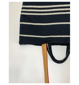 Detail of navy canvas tote bag with white stripes and red-edged brown leather strap