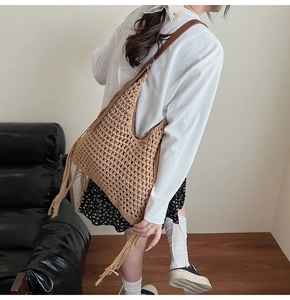 Close-up of a khaki woven straw tote bag with long fringe tassels and leather shoulder strap