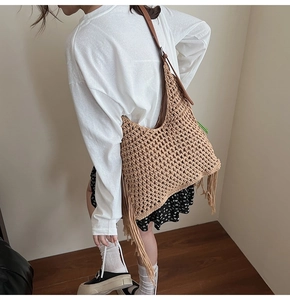 Detail of woven straw shoulder bag featuring bohemian tassels and brown leather straps