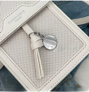 Detail view of cream crossbody bag featuring litchi leather, canvas and silver charm tassel