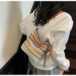 Detail of colorful striped knit hobo bag featuring brown leather strap and baseball charm