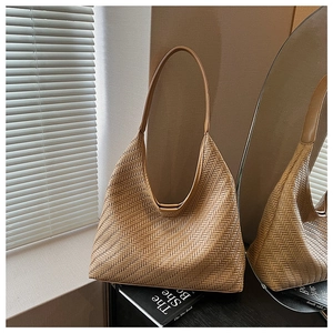 Detail of light brown woven tote bag showing fine texture and leather strap in soft sunlight
