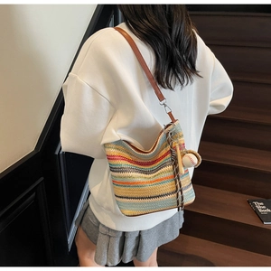 Detail of colorful striped woven tote bag featuring a leather strap and baseball charm