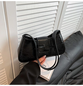 Detail of black crinkled patent leather shoulder bag with a slim bow on the front flap