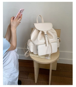 Detail view of cream white leather backpack with multiple zip pockets on a wooden stool