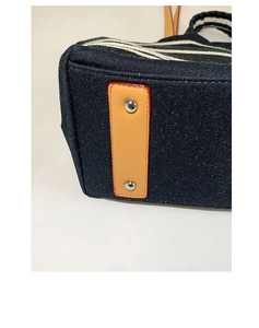 Detail of canvas tote bag showing striped fabric, brown leather trim with orange edge paint