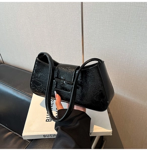 Close-up of black glossy wrinkled texture baguette bag with minimalist bow buckle detail