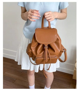 Brown faux leather backpack detail showing front zipper pocket and buckle flap closure