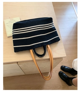 Close-up of a striped canvas tote bag with brown leather handles on a wooden table