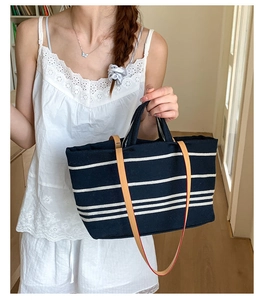 Detail of navy stripe canvas tote bag with brown leather handles worn by a model