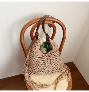 Detail of beige crochet tote bag with fringe tassels and leather strap on a chair
