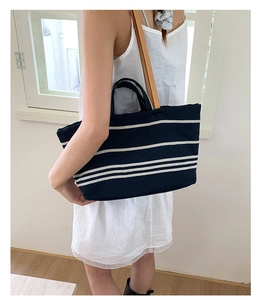Detail of navy striped canvas tote bag with brown leather straps shown on shoulder