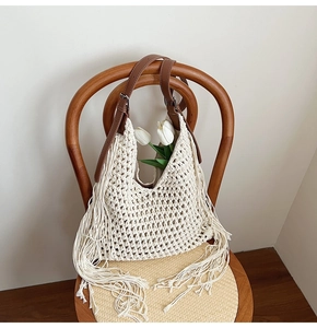 Detail of woven tote bag with fringe accents and brown leather adjustable strap