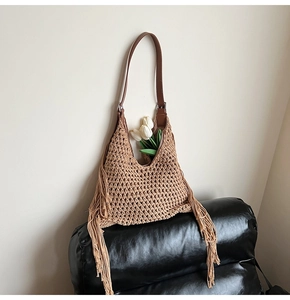Close-up of woven straw tote bag with long side tassels and brown leather shoulder strap