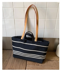 Close-up of striped canvas tote bag with brown faux leather handles on wooden table