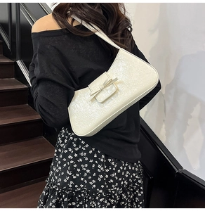 Detailed view of white patent leather shoulder bag with decorative bow and crinkle texture