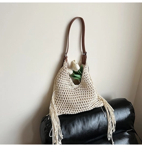 Detail of handmade woven bag with cream fringe and brown leather strap on black base