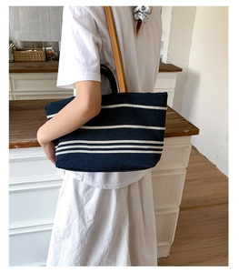 Detail of striped canvas tote bag with brown leather straps shown in a lifestyle setting