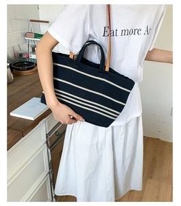 Navy blue striped canvas tote bag with brown leather handles worn by a model