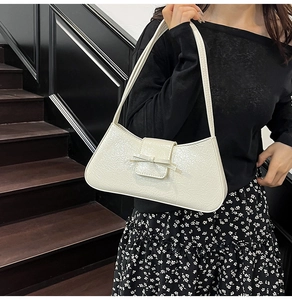 Detail of a creamy white hobo bag with glossy pleated texture and a decorative bow