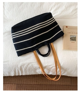 Detail of striped canvas tote bag with brown leather handles on white bedding backdrop