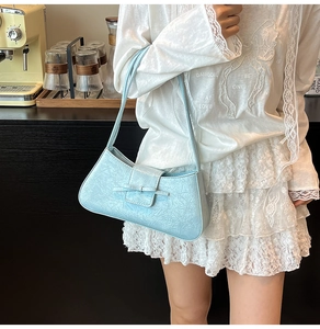 Detail of light blue pleated shoulder bag with bow decoration in a cafe setting