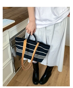 Detail of striped canvas tote bag with brown leather handles and large storage space