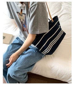 Detail of navy blue canvas tote bag with white stripes and brown leather handles