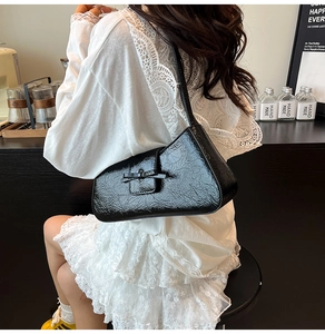 Detail of black pleated hobo bag with a delicate bow and glossy finish on the shoulder strap