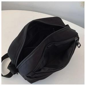 Detail view of black nylon crossbody bag showing multiple zippered compartments and storage