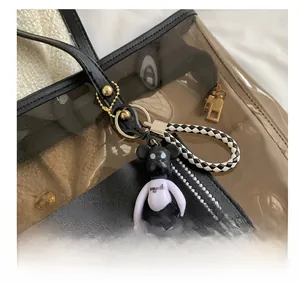 Détail d'un ours porte-clés avec chemise violette sur un sac fourre-tout en cuir noir