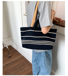 Detail of striped canvas tote bag showing dual straps and large capacity worn by a model