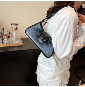 Detailed close-up of black glossy pleated shoulder bag with a stylish ribbon detail