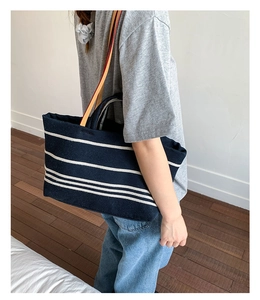 Navy canvas tote bag with white stripes and orange strap shown on model in home setting