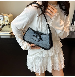 Detailed view of black crocodile pattern underarm bag worn by model in casual setting