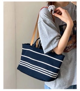 Detail of striped canvas tote bag showing dark blue body and brown leather handles