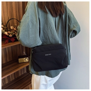 Detail of minimalist black nylon crossbody bag with DAI OU logo worn by model in home setting