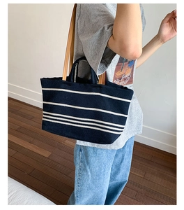 Detail of navy canvas tote bag with white stripes and brown leather handle and shoulder strap