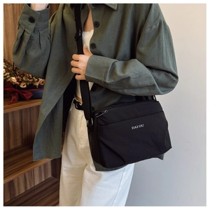 Detail of adjustable strap and white logo on black nylon waterproof crossbody bag