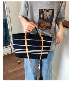 Close-up of navy blue striped canvas tote bag with leather straps on a casual model