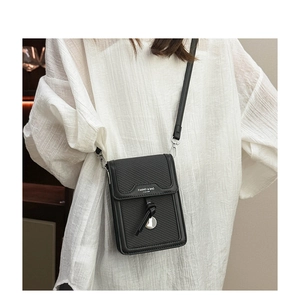 Detail of black crossbody phone bag with woven texture and silver metal charm on model