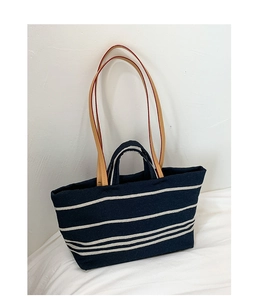 Detail of striped canvas tote with brown leather handles on soft white fabric