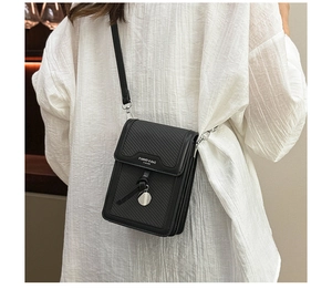 Detail of a black leather crossbody phone bag with textured flap and metal pendant