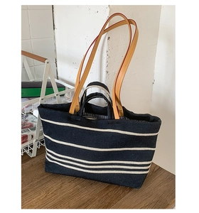 Close-up of navy canvas tote bag with white stripes and brown leather shoulder straps