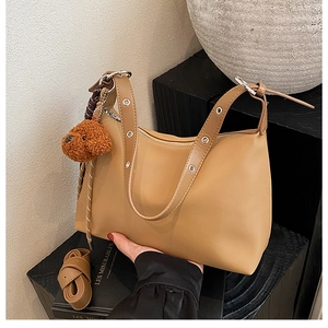 Détail du sac bandoulière camel avec œillets argentés et breloque ours en peluche