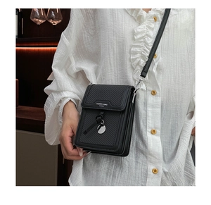 Close-up of small black crossbody bag featuring woven texture and metallic logo detail