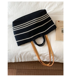 Overhead view of a navy blue striped canvas tote bag with brown leather straps on white fabric