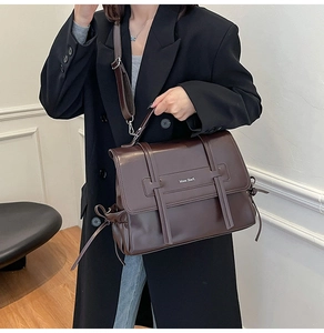 Detail of vintage dark brown faux leather messenger bag with metal logo and wide strap